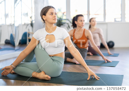 Girl teacher conducts lesson, training for girls in yoga studio and performs Lord of fishes pose. Girl teacher conducts lesson, training for girls in yoga studio and performs Lord of fishes pose. 137058472