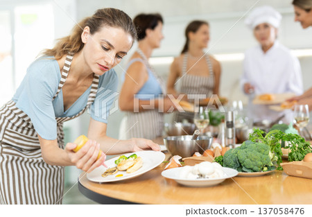 Girl visitors to culinary school decorates finished dish, fried chicken fillet with golden crust. 137058476