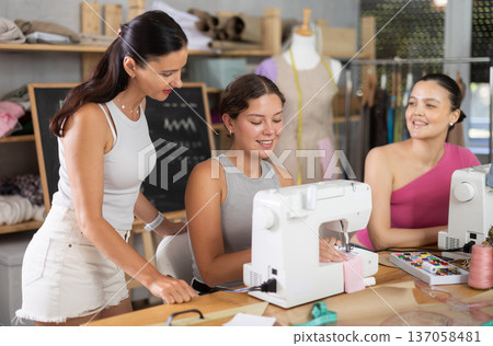 Smiling girl stitching fabric on machine in sewing class for adults 137058481