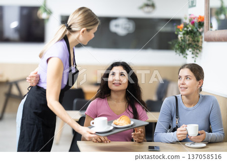 Girl waiter in apron presents coffee and croissants to restaurants guests. Girl waiter in apron presents coffee and croissants to restaurants guests. 137058516