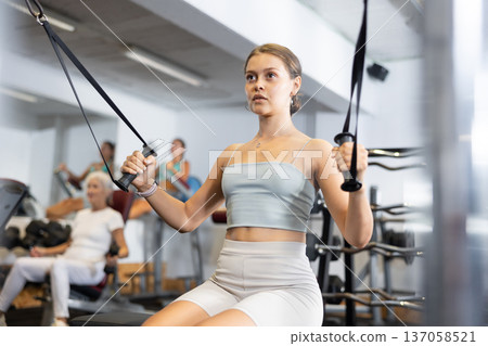 Athletic woman working on special machine with ropes to develop arm muscles 137058521