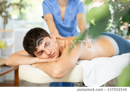Masseuse doing back massage to young guy Masseuse doing back massage to young guy 137058548