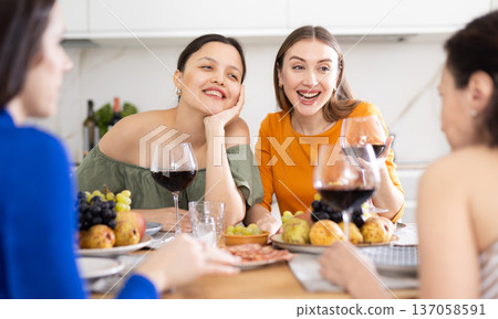 Girlfriends chatting and drinking wine in kitchen Girlfriends chatting and drinking wine in kitchen 137058591