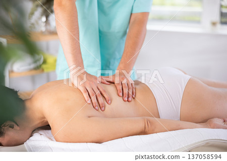 Masseur doing back massage to adult woman Masseur doing back massage to adult woman 137058594