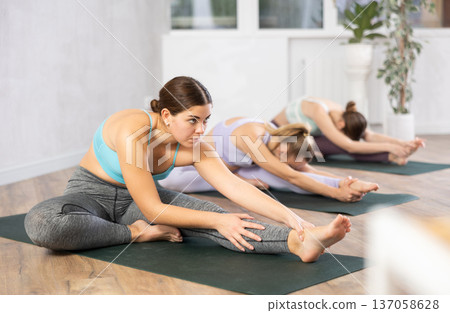 Diligent women practicing head to knee pose of yoga in light fitness room Diligent women practicing head to knee pose of yoga in light fitness room 137058628