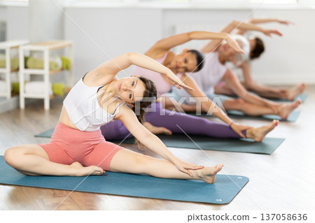 Girl stretching in Parivrtta Janu Sirsasana at group yoga training Girl stretching in Parivrtta Janu Sirsasana at group yoga training 137058636