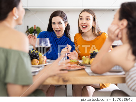 Four women are sitting at table, enjoying food and wine, chatting, talking, laughing. 137058643