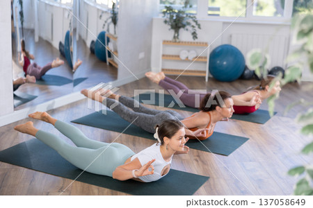 Sportive women performing cobra pose of yoga during group training in training room Sportive women performing cobra pose of yoga during group training in training room 137058649