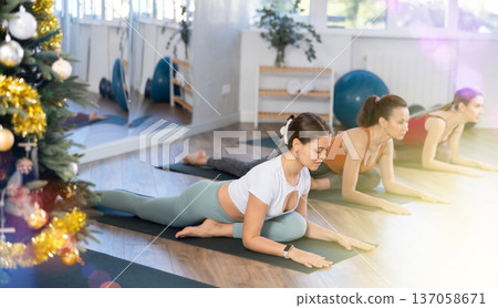 Young beautiful girl with other people relaxing and enjoying yoga in fitness center during Christmas holidays 137058671