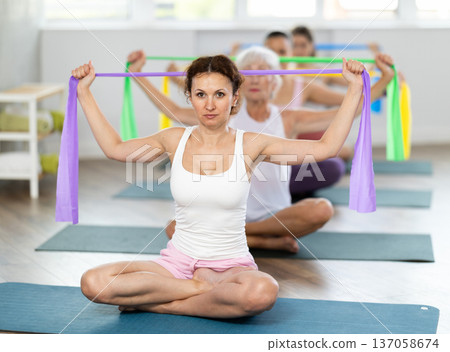 Woman exercising with resistance band in group fitness class Woman exercising with resistance band in group fitness class 137058674
