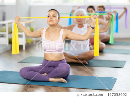 Group Pilates classes - woman doing body stretching using elastic bands in gym 137058692