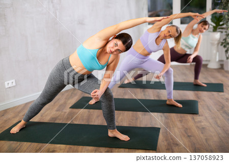 Sporty young girl practicing stretching during group yoga class Sporty young girl practicing stretching during group yoga class 137058923