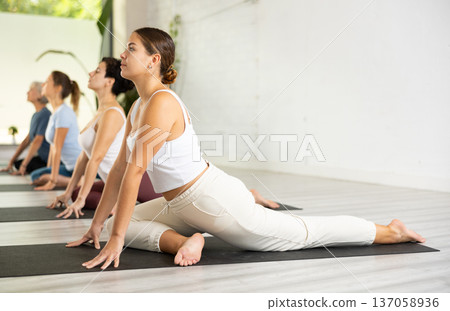 Sporty female doing stretching workout during group training in fitness studio 137058936