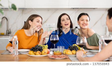 Girlfriends drinking wine and having conversation over dinner at house party Girlfriends drinking wine and having conversation over dinner at house party 137058943