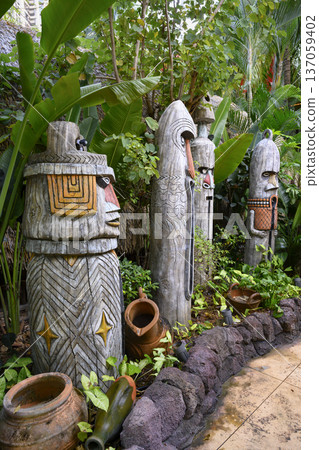 Wooden carved idols and clay pots among tropical flowers in the city park in Sania, China Wooden carved idols and clay pots among tropical flowers in the city park in Sania, China 137059402