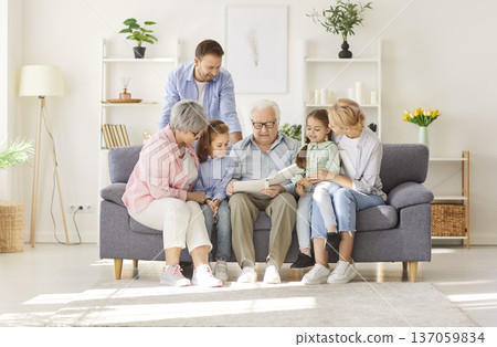 Grandfather, grandmother, mother, father and children sitting on sofa and reading book together 137059834