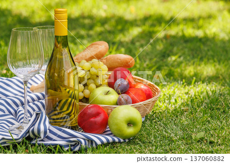 Picnic with wine, fruits, and baguette on a green meadow 137060882