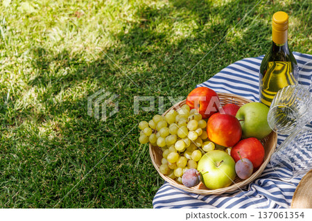 Picnic with wine, fruits, and baguette on a green meadow Picnic with wine, fruits, and baguette on a green meadow 137061354