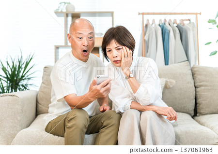 Middle-aged Asian couple sitting on the sofa in the living room at home and looking at their smartphone (surprised, surprised, trouble) Middle-aged Asian couple sitting on the sofa in the living room at home and looking at their smartphone (surprised, surprised, trouble) 137061963