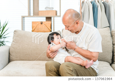 笑容滿面的爺爺抱著孫子，用奶瓶餵他。 137061964