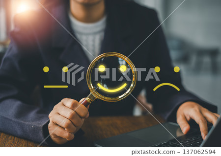Professional analyzing customer satisfaction using emoticons and magnifying glass, highlighting feedback and review process. 137062594