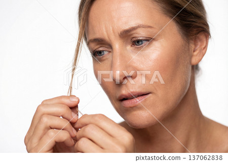 Middle aged woman examining hair strand with worried expression 137062838