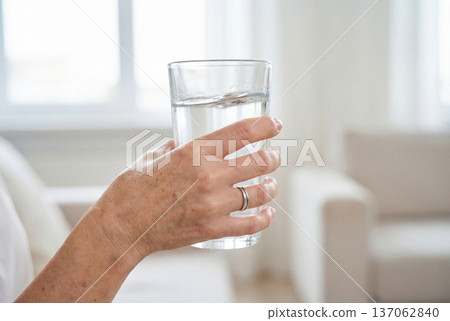 Middle aged woman hand holding glass of water with shaking tremor 137062840
