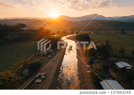Aerial view of a winding river through a rural village and camping site with a beautiful golden sunset and mountains in the background. Aerial view of a winding river through a rural village and camping site with a beautiful golden sunset and mountains in the background. 137063249