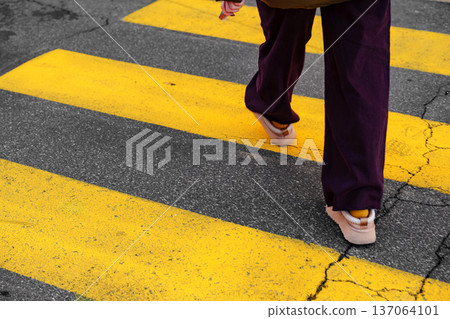 Person walks on yellow crosswalk lines in urban area on a clear day 137064101