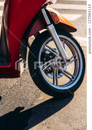 Red scooter parked on the street showing wheel and tire in the afternoon light 137064114