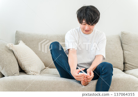 Young Asian man sitting on sofa and cutting his toenails 137064355