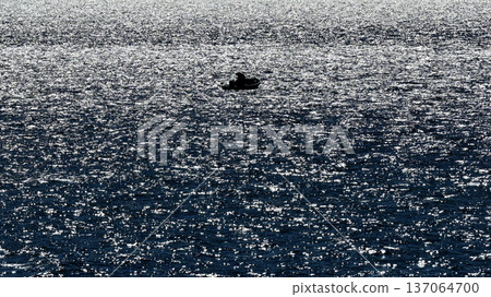 The sea sparkling in the backlight and the silhouette of a fisherman in a small boat The sea sparkling in the backlight and the silhouette of a fisherman in a small boat 137064700