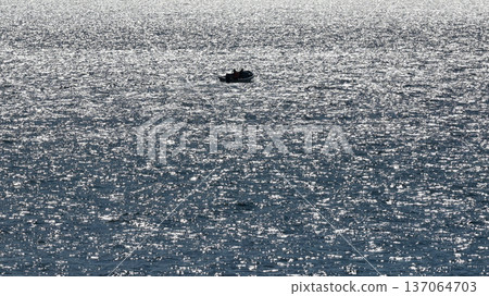 逆光下波光粼粼的海面，以及小船上漁夫的剪影。 137064703
