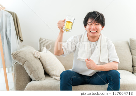 A young Asian man sitting on a sofa after taking a bath and drinking beer from a mug A young Asian man sitting on a sofa after taking a bath and drinking beer from a mug 137064718