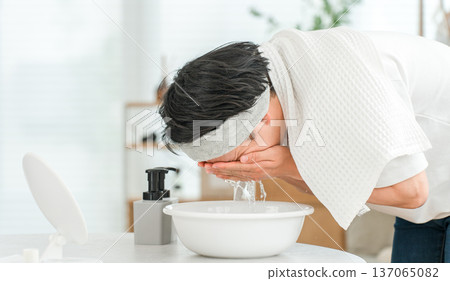 一名戴著髮帶的年輕亞洲男子正在洗臉。 一名戴著髮帶的年輕亞洲男子正在洗臉。 137065082