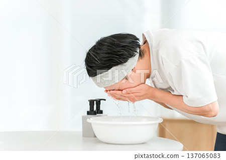 一名戴著髮帶的年輕亞洲男子正在洗臉。 137065083