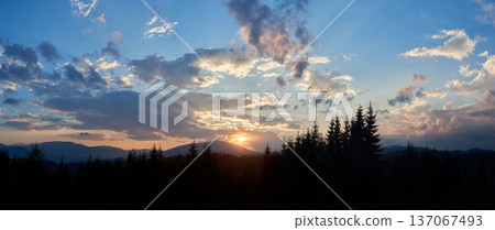 Sun sets behind range of distant mountains, casting golden rays through clouds. Sky, painted with shades of blue, pink, and gold, in tranquil evening. Silhouetted pine trees add depth to landscape. Sun sets behind range of distant mountains, casting golden rays through clouds. Sky, painted with shades of blue, pink, and gold, in tranquil evening. Silhouetted pine trees add depth to landscape. 137067493