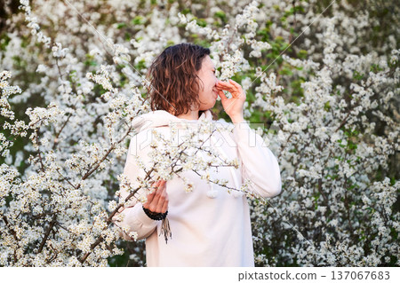 Woman allergic suffering from seasonal allergy at spring in blossoming garden at springtime. Young woman sneezing, closing nose by hand in front of blooming tree. Spring allergy concept Woman allergic suffering from seasonal allergy at spring in blossoming garden at springtime. Young woman sneezing, closing nose by hand in front of blooming tree. Spring allergy concept 137067683