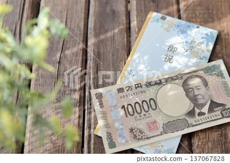 一個淺藍色花卉圖案的禮物信封和一張嶄新的10000日元鈔票。畢業禮物或畢業慶祝活動禮物。 一個淺藍色花卉圖案的禮物信封和一張嶄新的10000日元鈔票。畢業禮物或畢業慶祝活動禮物。 137067828