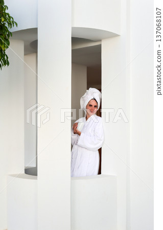 A woman in a robe and towel drinks a hot drink on a terrace after a shower A woman in a robe and towel drinks a hot drink on a terrace after a shower 137068107