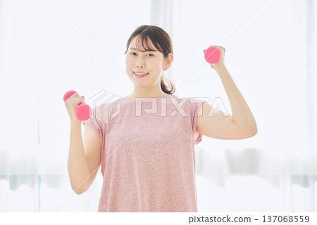 Home fitness and wellness lifestyle of a woman in her 30s doing dumbbell exercises at home 137068559