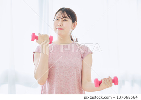 Home fitness and wellness lifestyle of a woman in her 30s doing dumbbell exercises at home Home fitness and wellness lifestyle of a woman in her 30s doing dumbbell exercises at home 137068564
