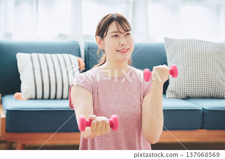 Home fitness and wellness lifestyle of a woman in her 30s doing dumbbell exercises at home 137068569