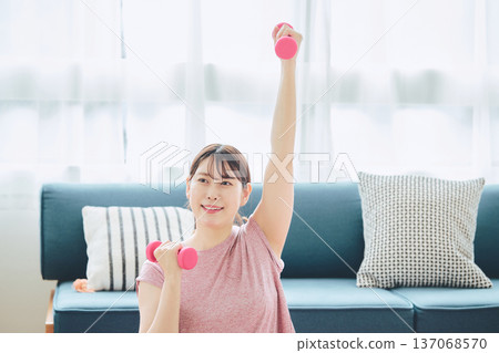 一位30多歲的女性在家中進行啞鈴鍛煉，展現了她的居家健身和健康生活方式。 137068570