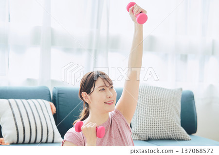 Home fitness and wellness lifestyle of a woman in her 30s doing dumbbell exercises at home 137068572
