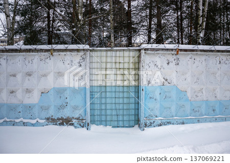 Winter scene with a weathered concrete fence topped with barbed wire and block gate 137069221