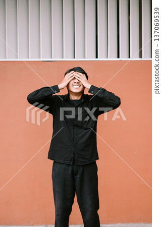 Young man covers his eyes with hands feeling overwhelmed Young man covers his eyes with hands feeling overwhelmed 137069539