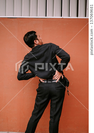 Young man experiencing lower back pain against orange wall Young man experiencing lower back pain against orange wall 137069681