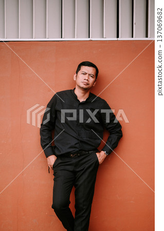 Confident Asian Man Leaning Against Textured Orange Wall Confident Asian Man Leaning Against Textured Orange Wall 137069682