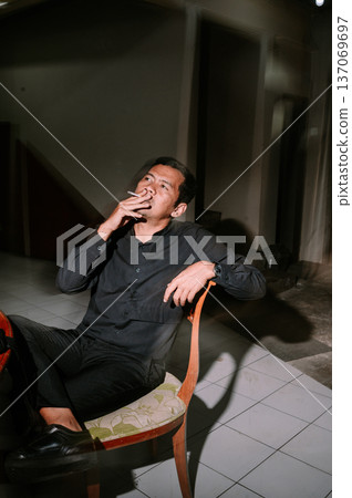 Pensive Man Smoking Cigarette in Dimly Lit Room Pensive Man Smoking Cigarette in Dimly Lit Room 137069697